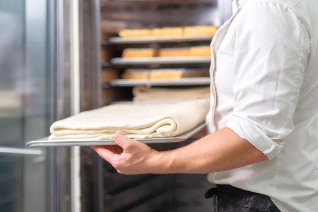 Man putting dough in a commercial bakery refrigerator