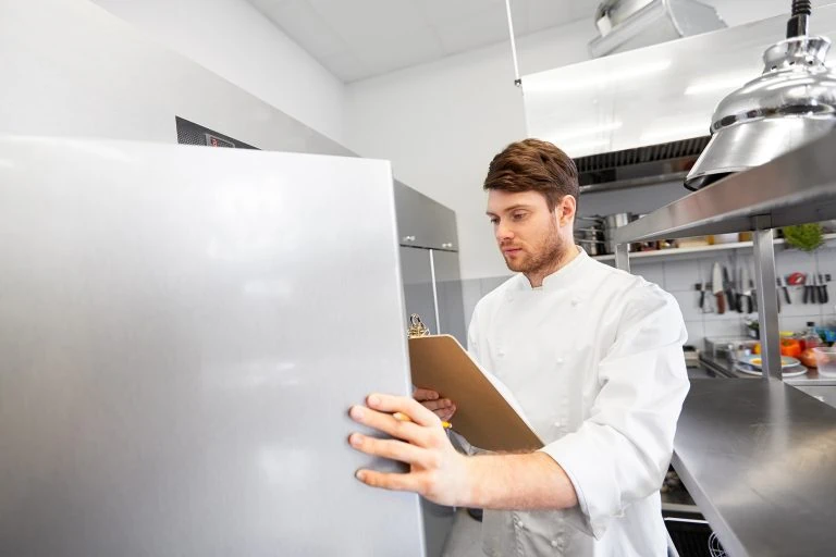 Professional male chef holding a clipboard while checking out a commercial fridge