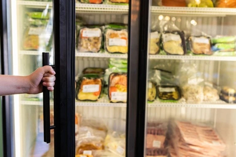 Hand holding the handle of a commercial display fridge displaying packaged food