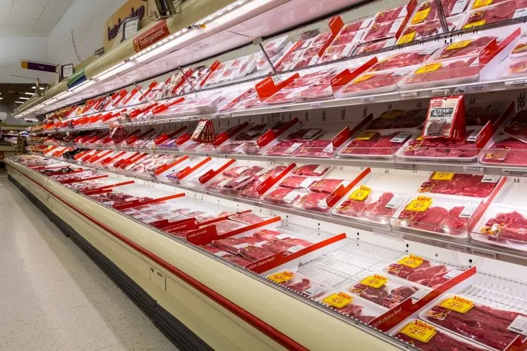 Open air reach in commercial refrigerator displaying packages of raw meat