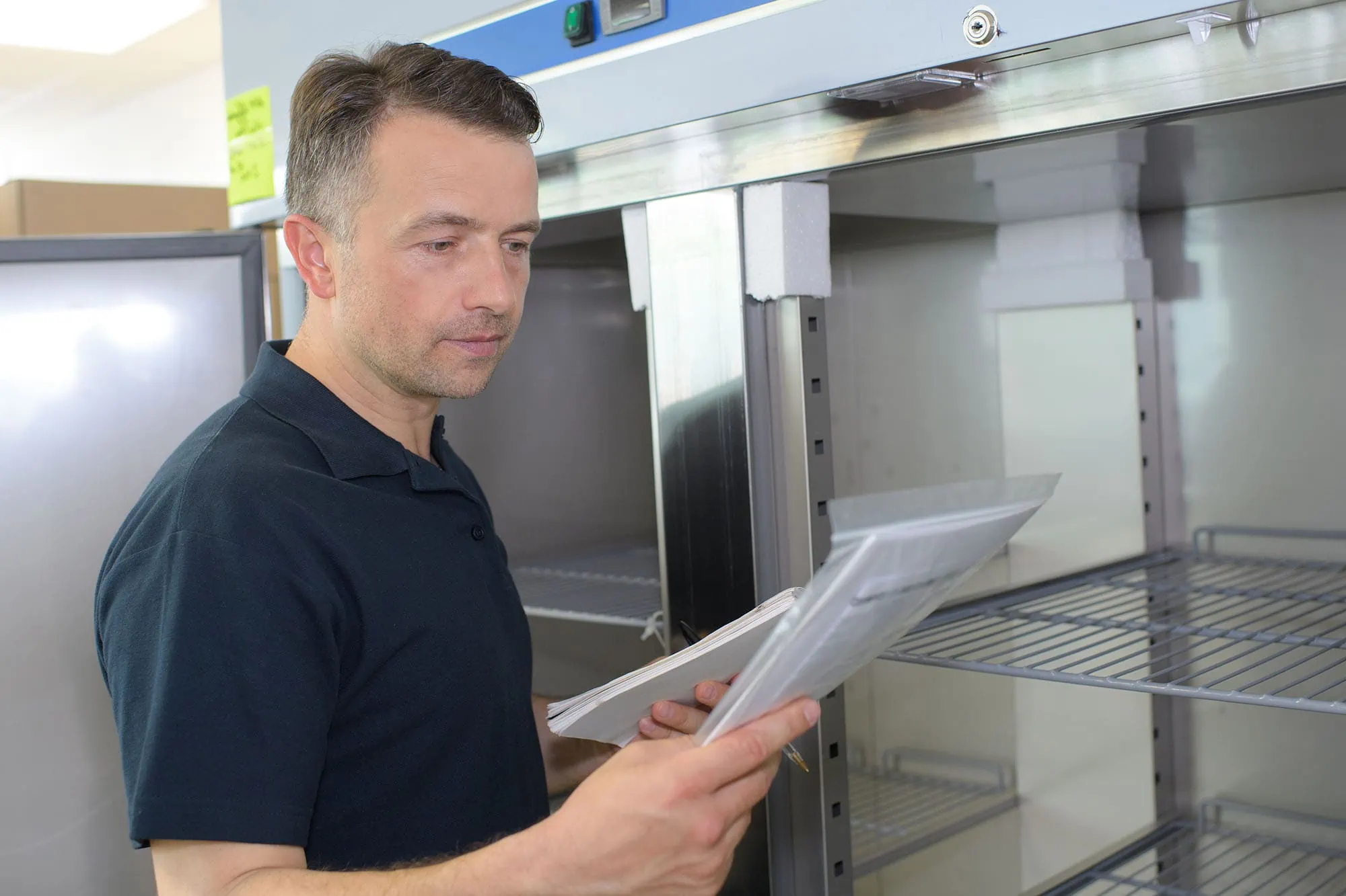 Man consulting a checklist while inspecting a commercial refrigerator