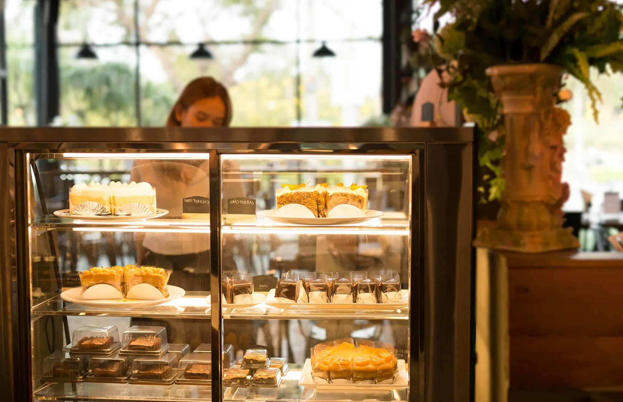 Woman selecting a pastry from a display fridge in a coffee shop